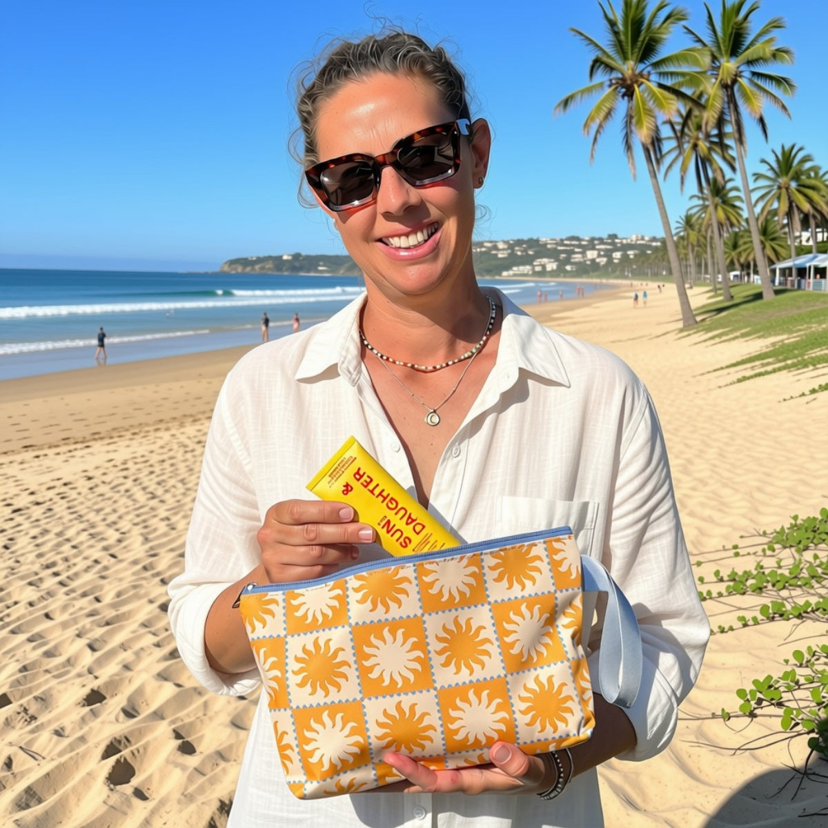 Smiling woman on the beach holding the Golden Rays pouch